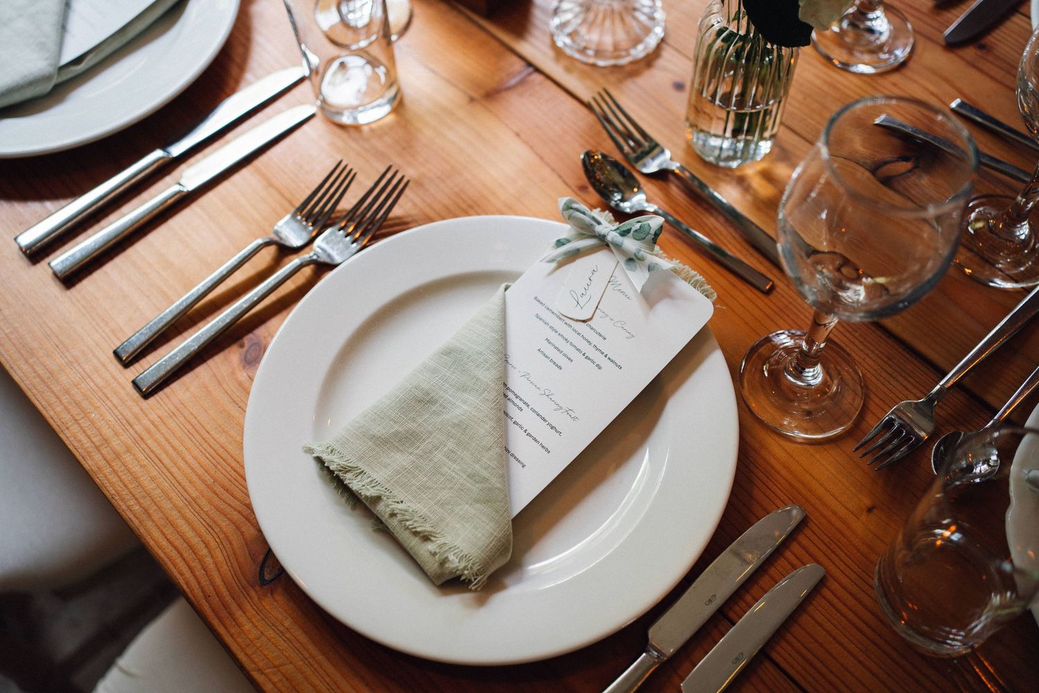 Place settings at a rustic wooden dining table with white plates, silverware, and glassware.