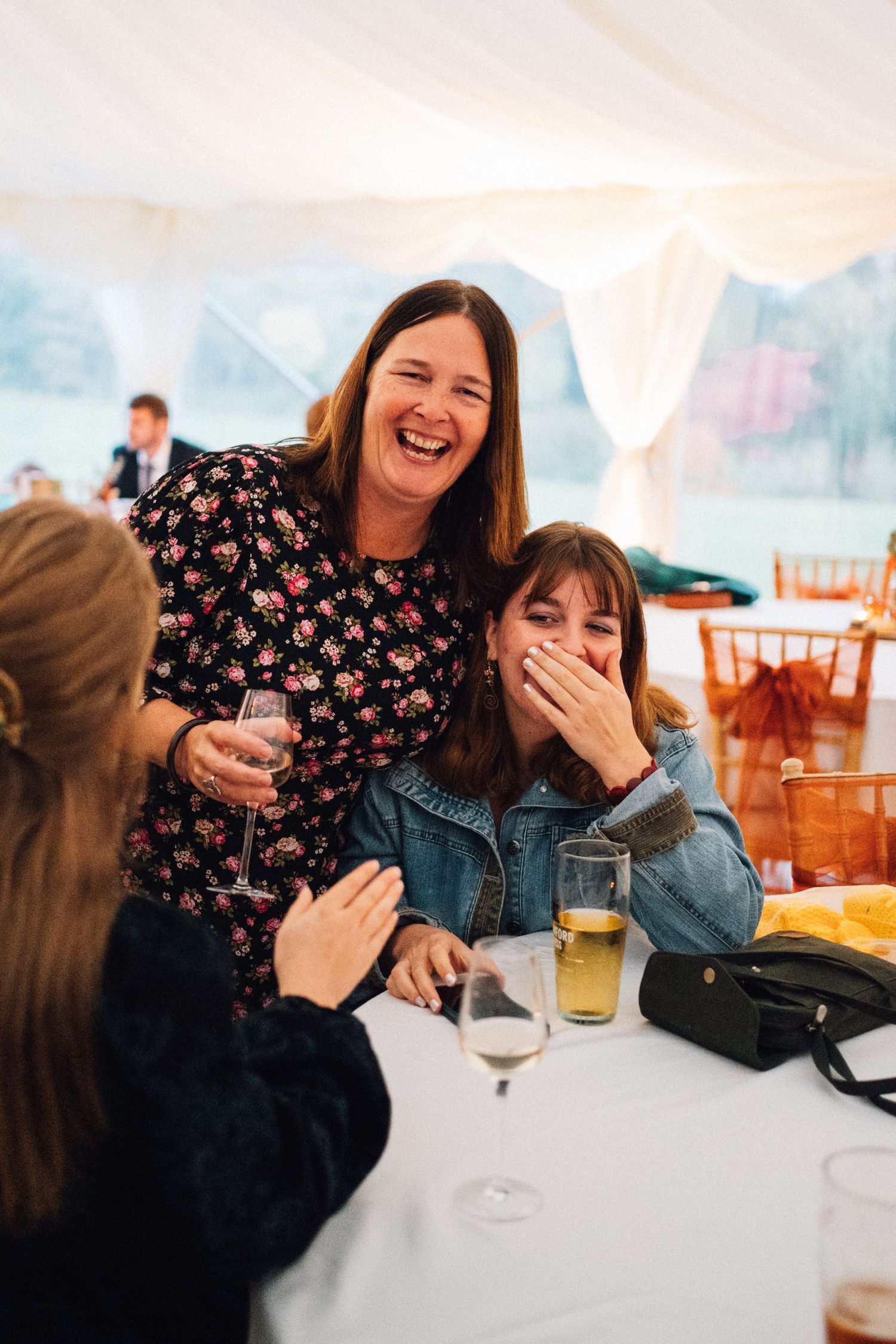 Two friends share a joyful moment while laughing together at a restaurant table with drinks.