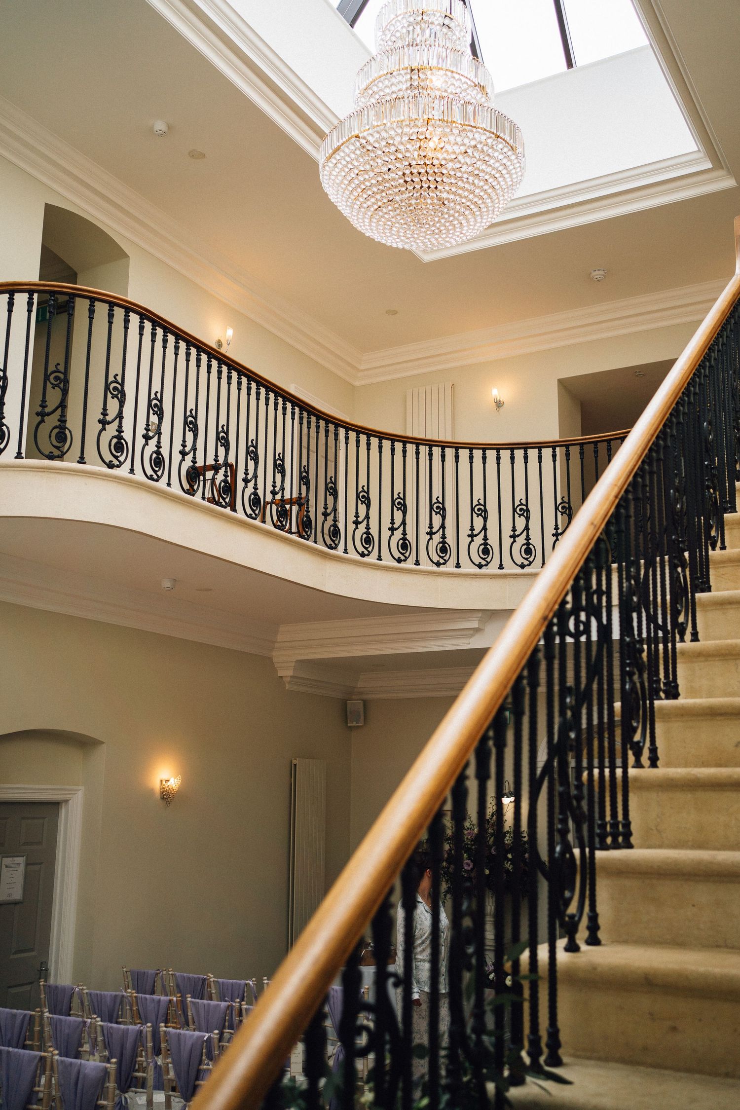 Elegant staircase with crystal chandelier and black wrought iron railings in luxury home interior.