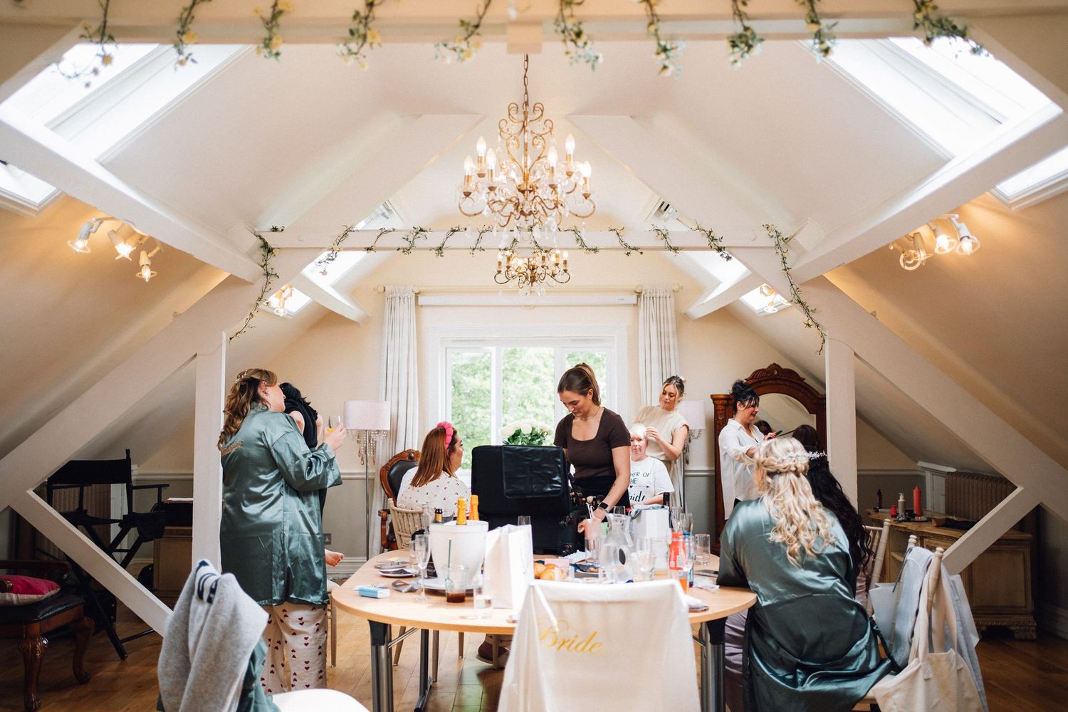Wedding guests gather in a bright attic reception space with exposed beams and a crystal chandelier.