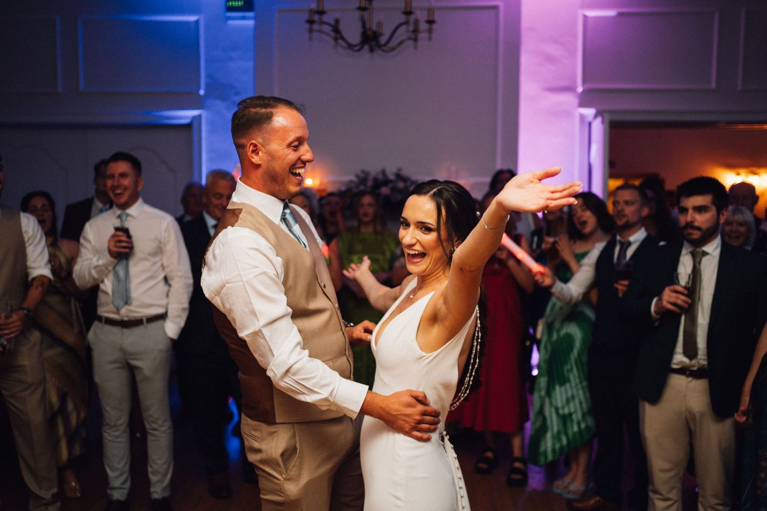 Wedding guests dance and celebrate on a colorfully lit dance floor during an evening reception.