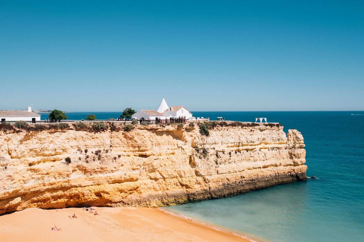 Scenic Mediterranean coastline with rocky cliffs and white buildings overlooking turquoise waters.