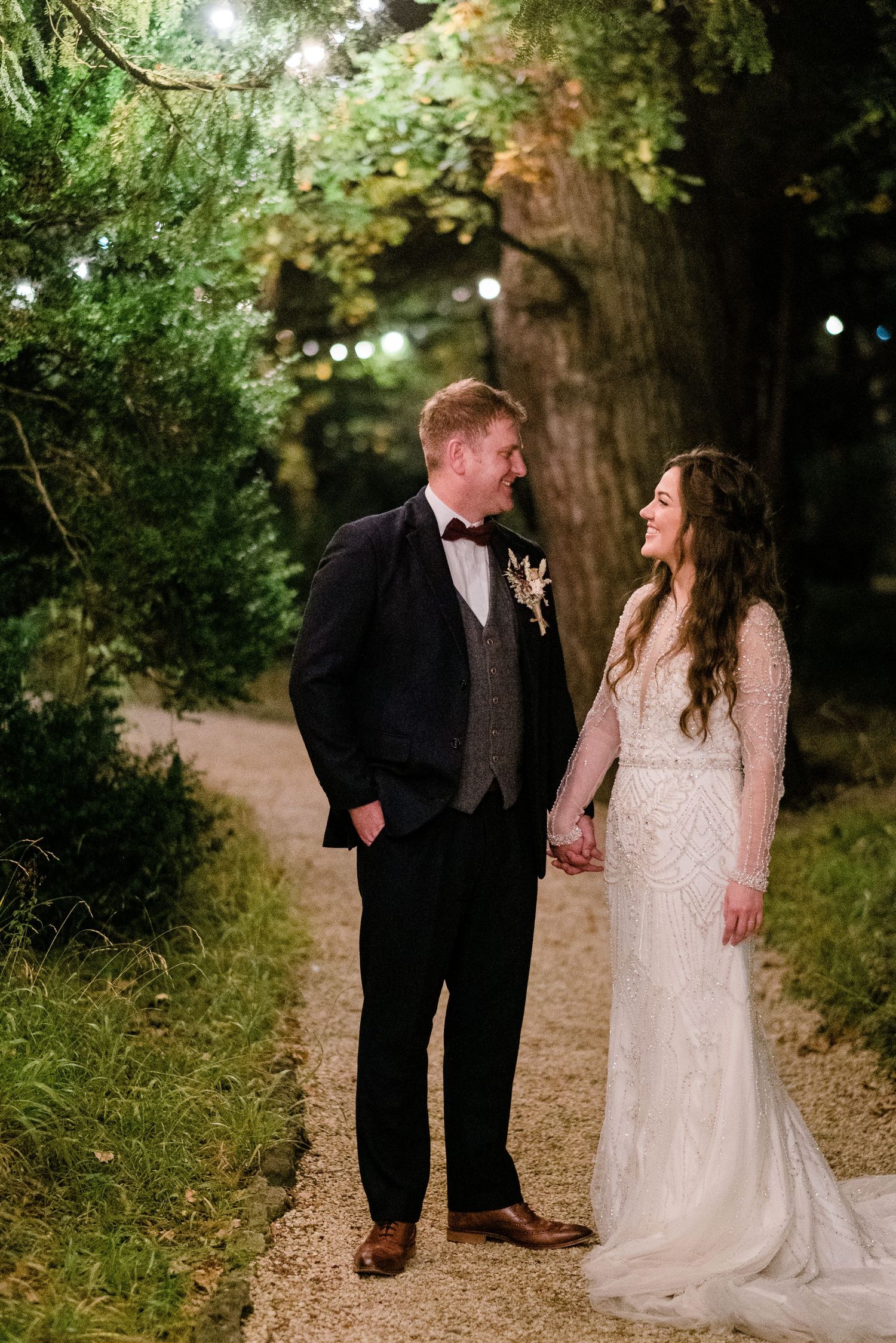 Wedding portraits captured on romantic garden path with string lights overhead.