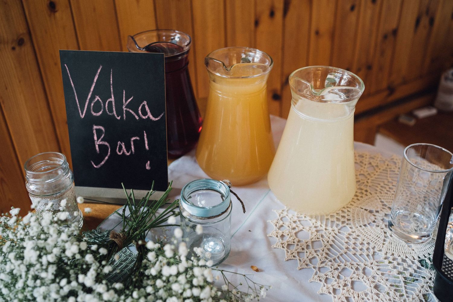 Wedding bar setup with drinks and baby's breath flowers on lace tablecloths.