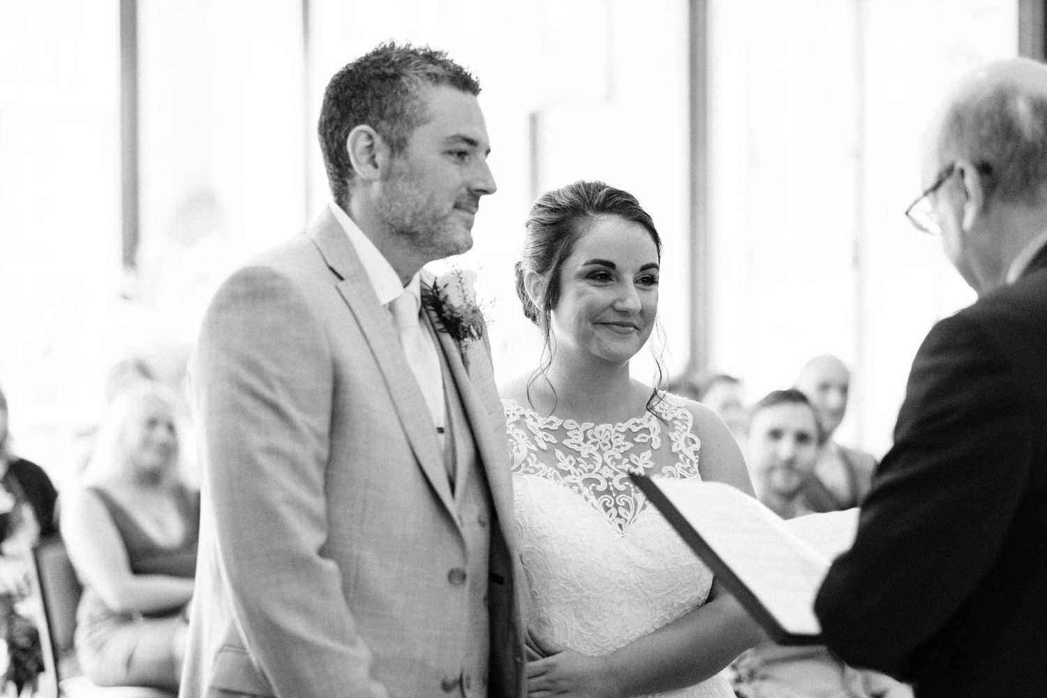 Wedding ceremony guests gather in an elegant white-draped venue with hanging lanterns.