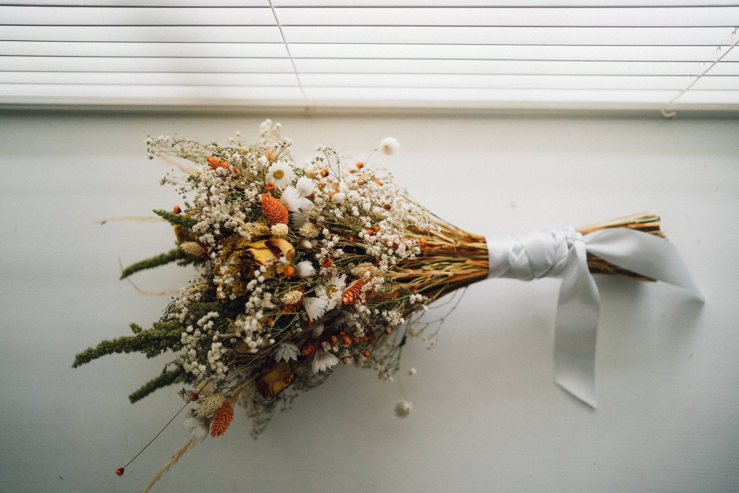 Dried floral arrangements in white vases displayed against a minimalist background.