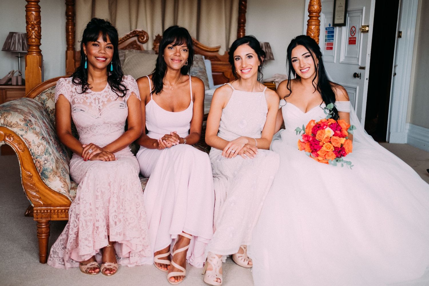 Wedding party in blush pink dresses poses together in an ornate room.