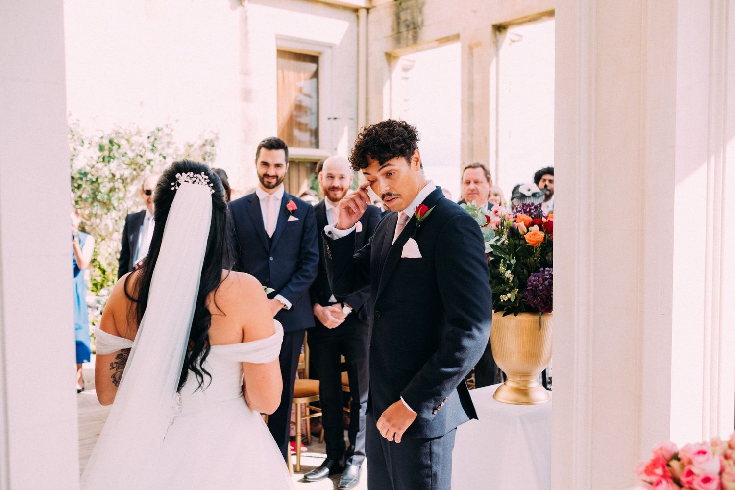 An intimate wedding ceremony moment captured in a sunlit room with white pillars.