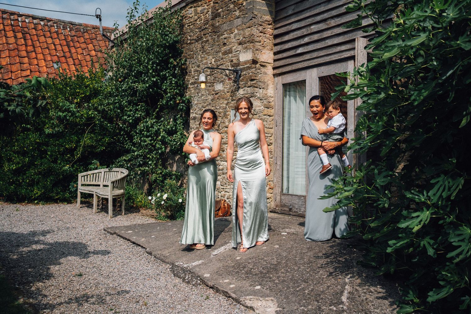 Wedding party posing outside rustic brick building with garden landscaping.
