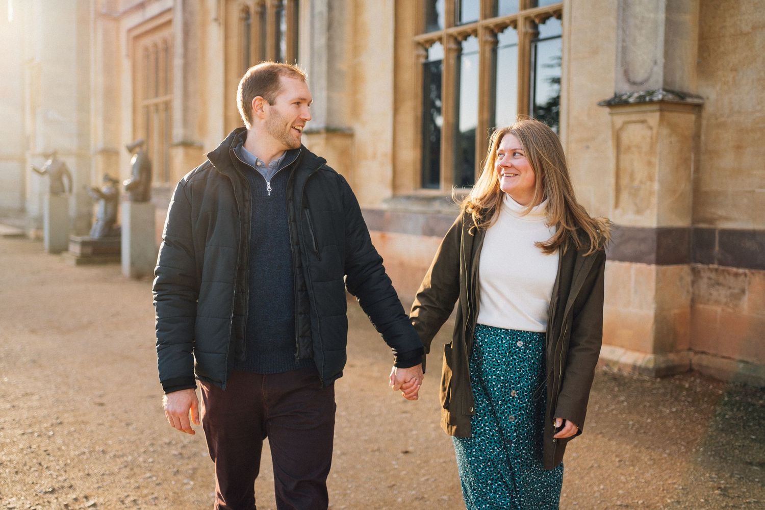 Couple in casual attire walking together outside a beautiful stone building.
