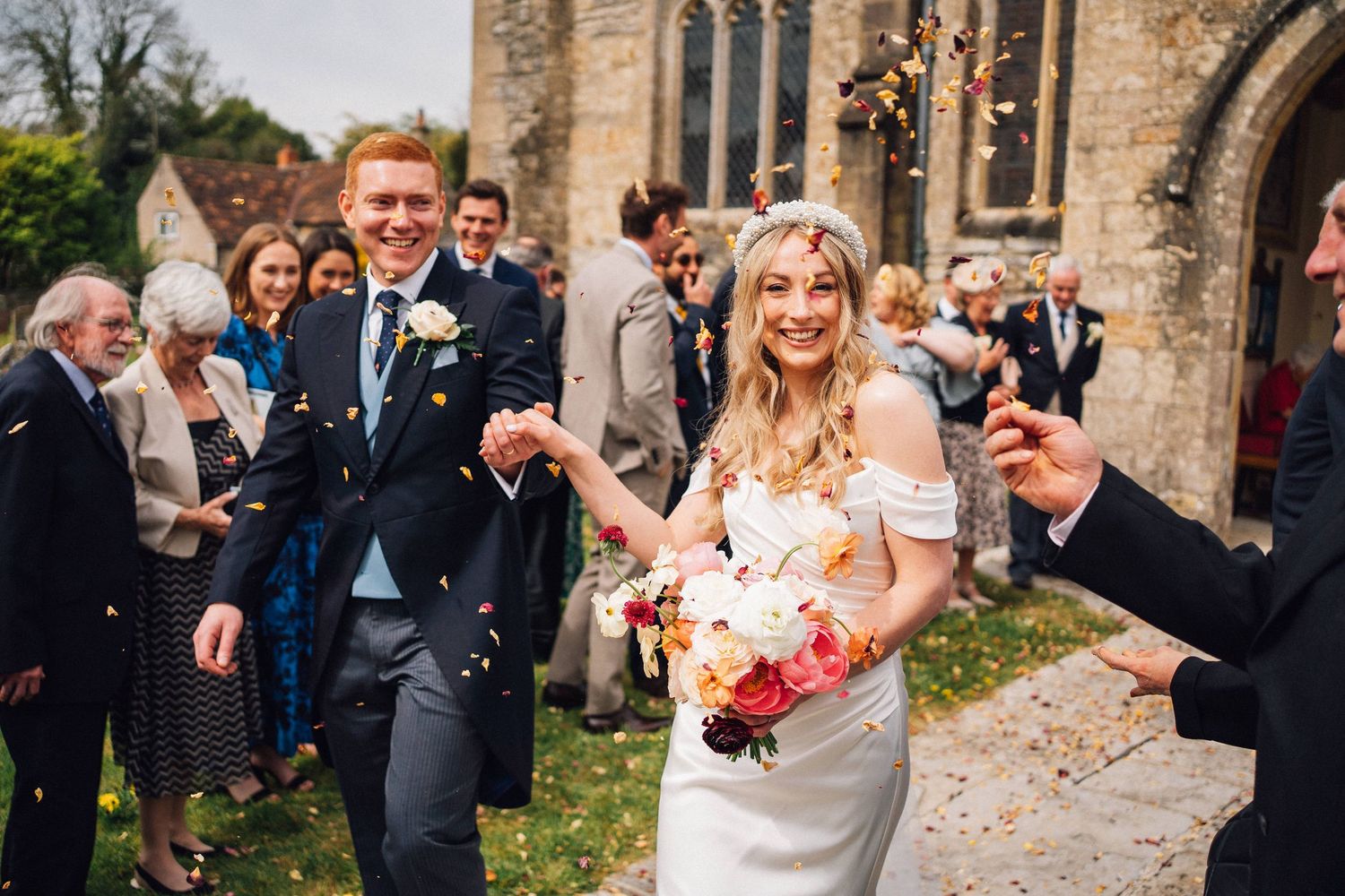 Wedding party celebrating with confetti outside historic stone church.