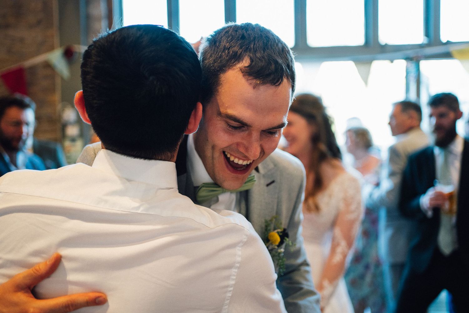 Celebration scene at a wedding reception showing guests interacting in a brick-walled venue.