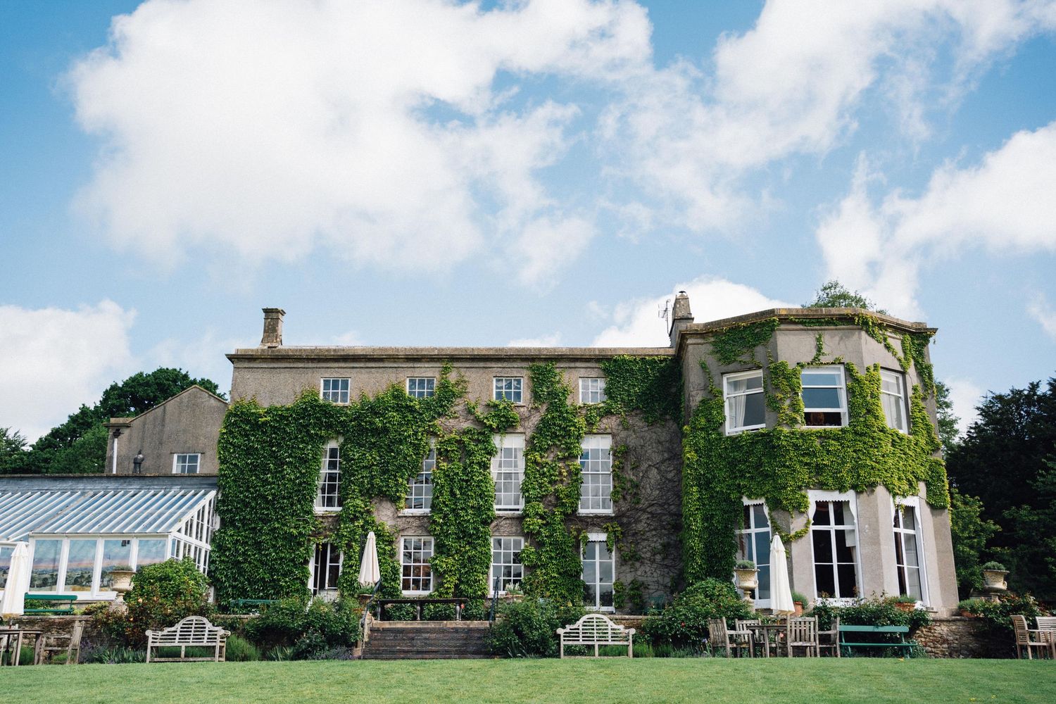 Ivy-covered English country manor house with manicured lawns, garden furniture, and blue skies, ideal wedding venue.