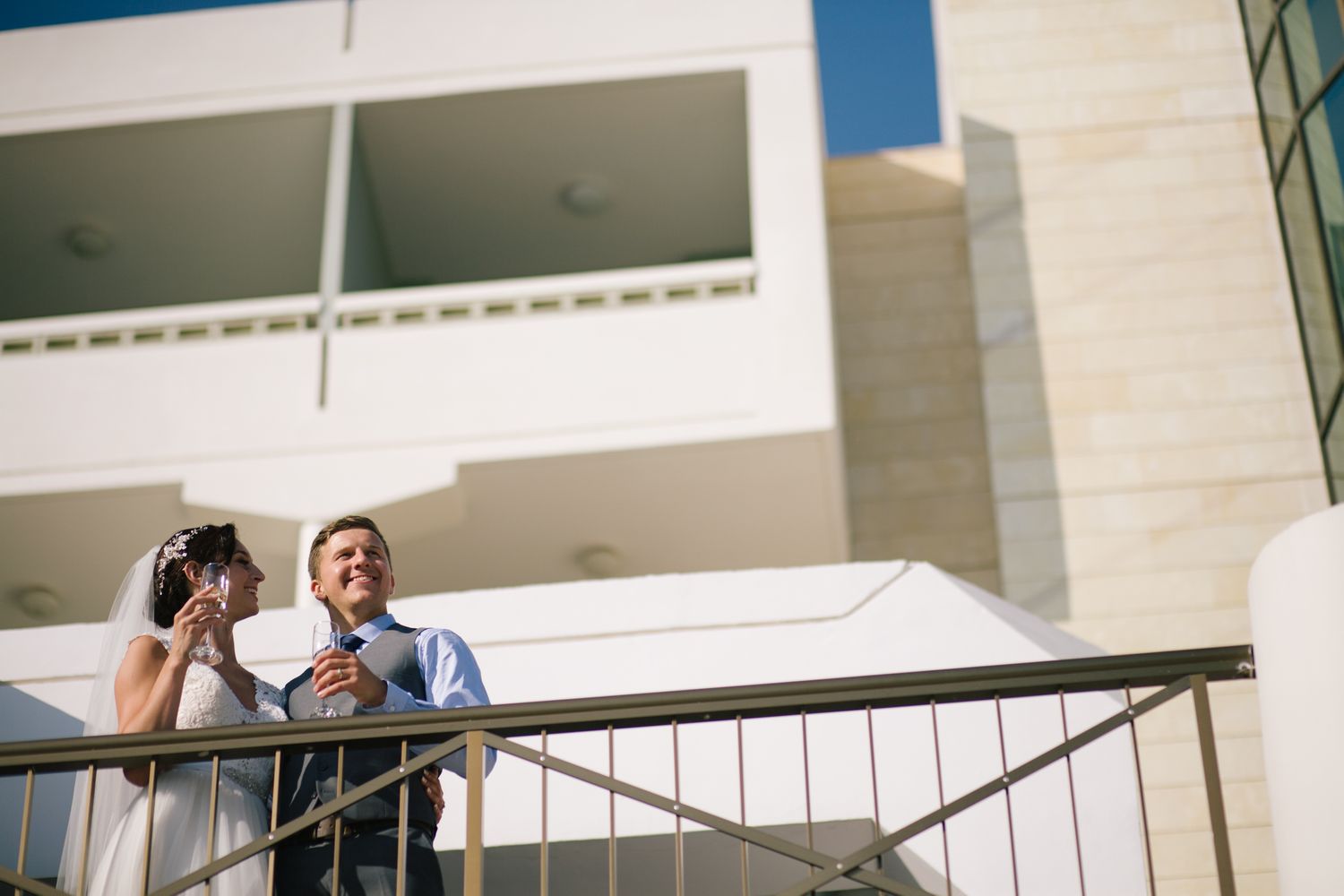 A candid moment shared between a couple on a balcony during their wedding day.