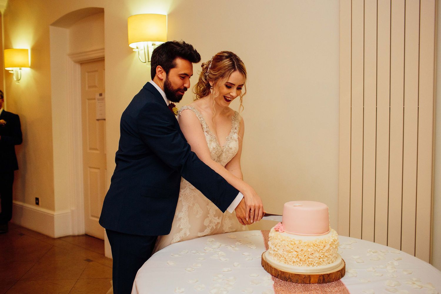 Wedding cake display featuring a pink and gold tiered cake in an elegantly lit venue.