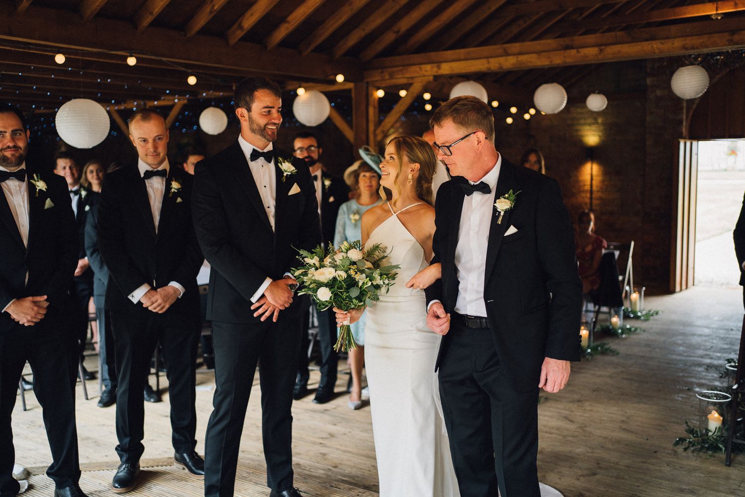 Wedding ceremony setup in a rustic barn with exposed beams and white paper lantern decorations.