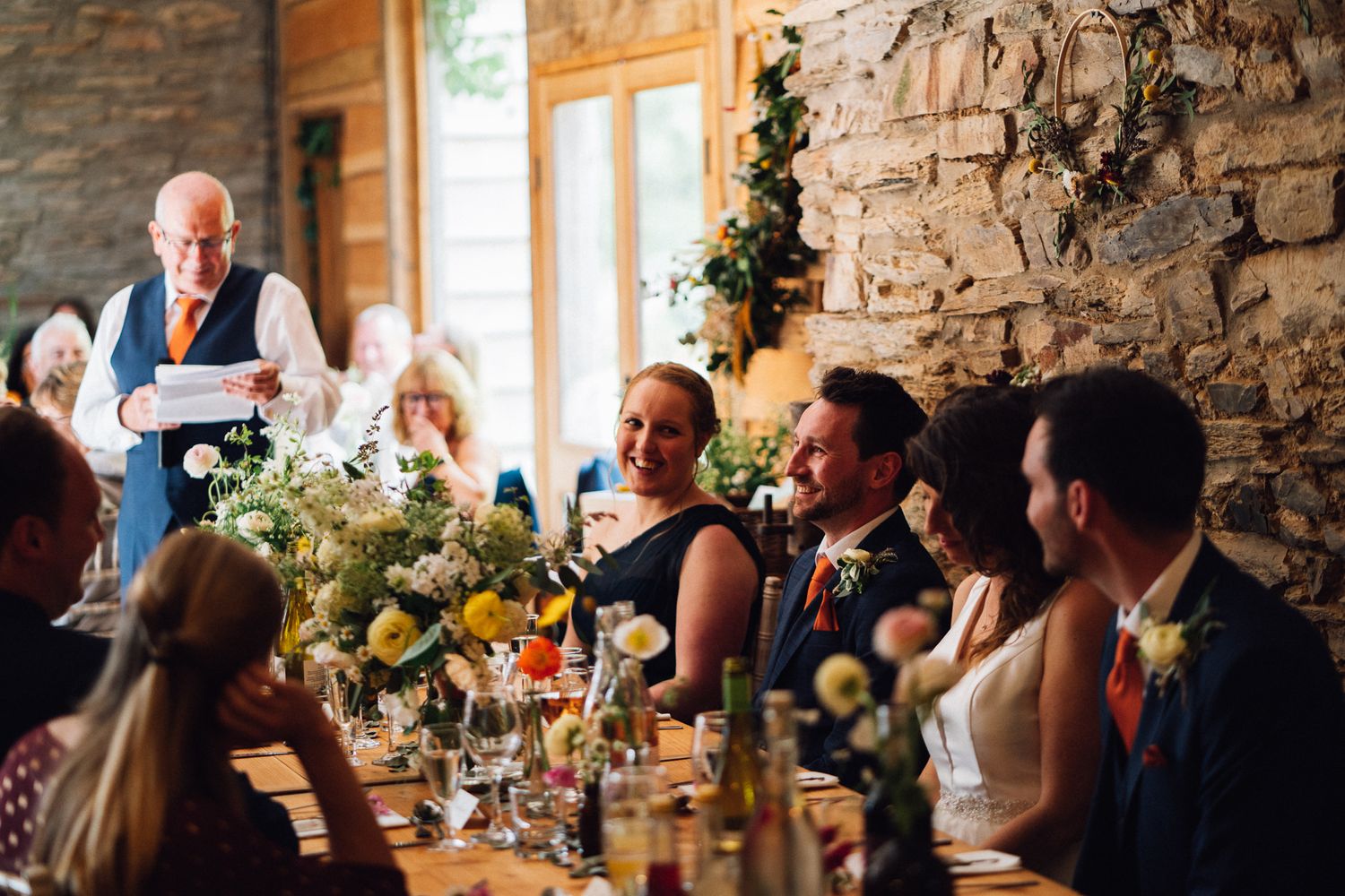 Wedding reception dinner in a rustic stone venue with natural light streaming through windows.