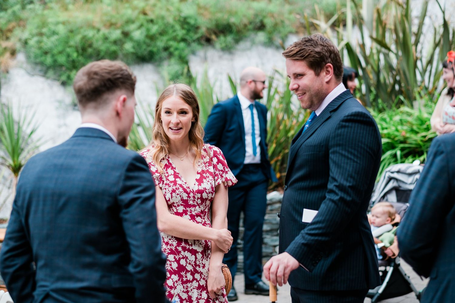Wedding guests mingling outdoors in a lush garden setting with floral decorations.