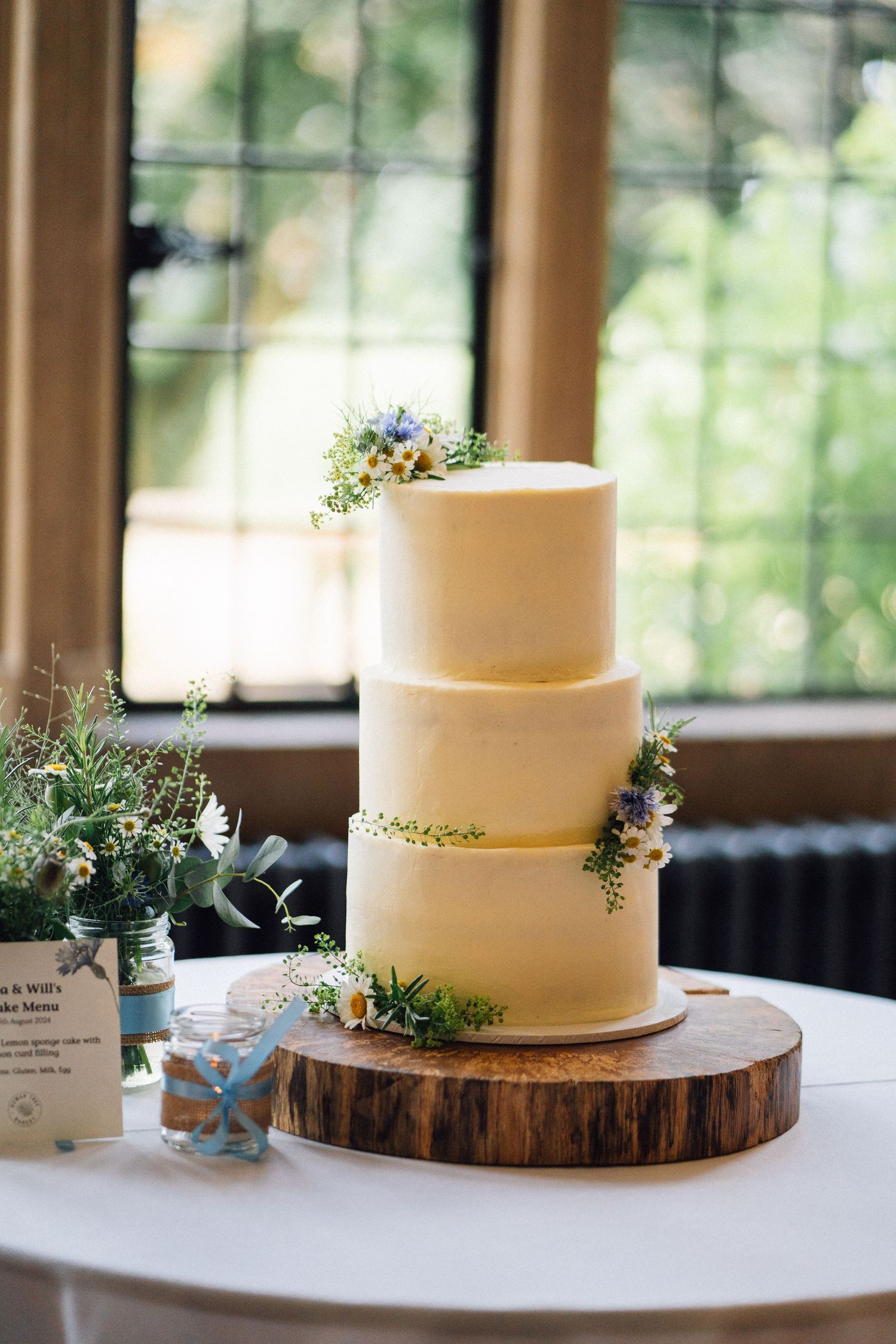 Simple white wedding cake displayed on rustic wood slice with delicate floral accents.