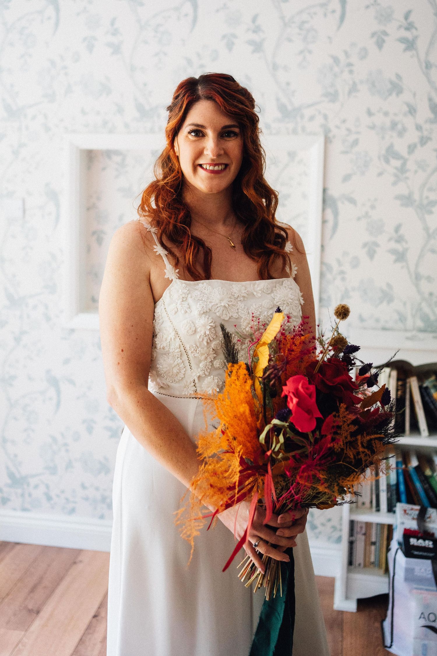 Autumn-inspired bridal bouquet features vibrant orange and deep red flowers with cascading foliage.