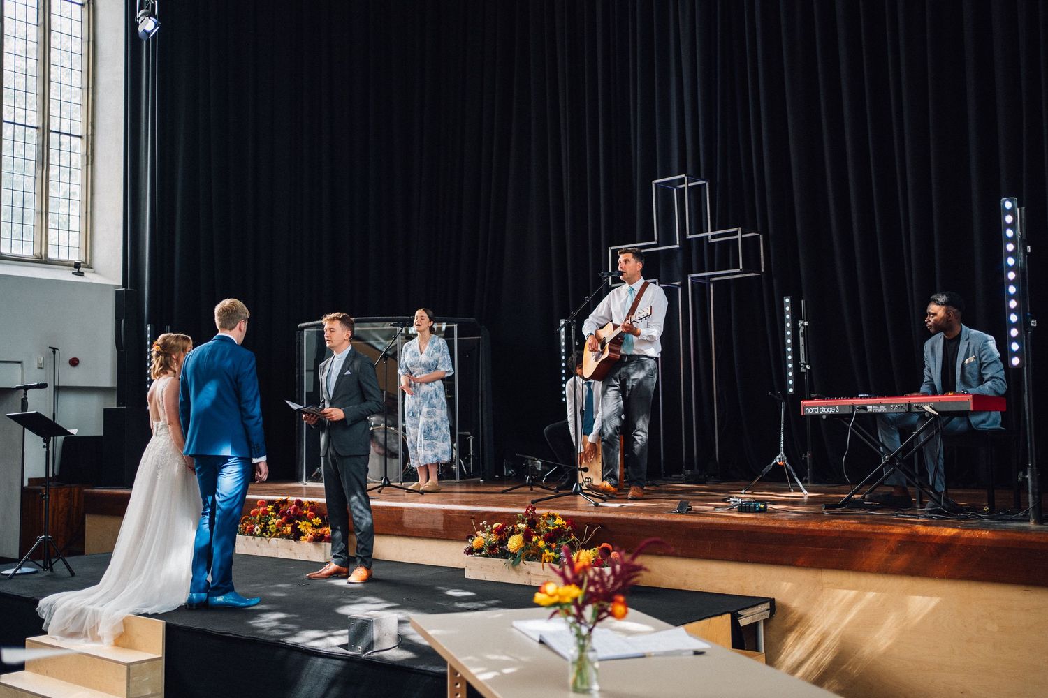 A worship band performs on stage with instruments and a cross backdrop during a church service.