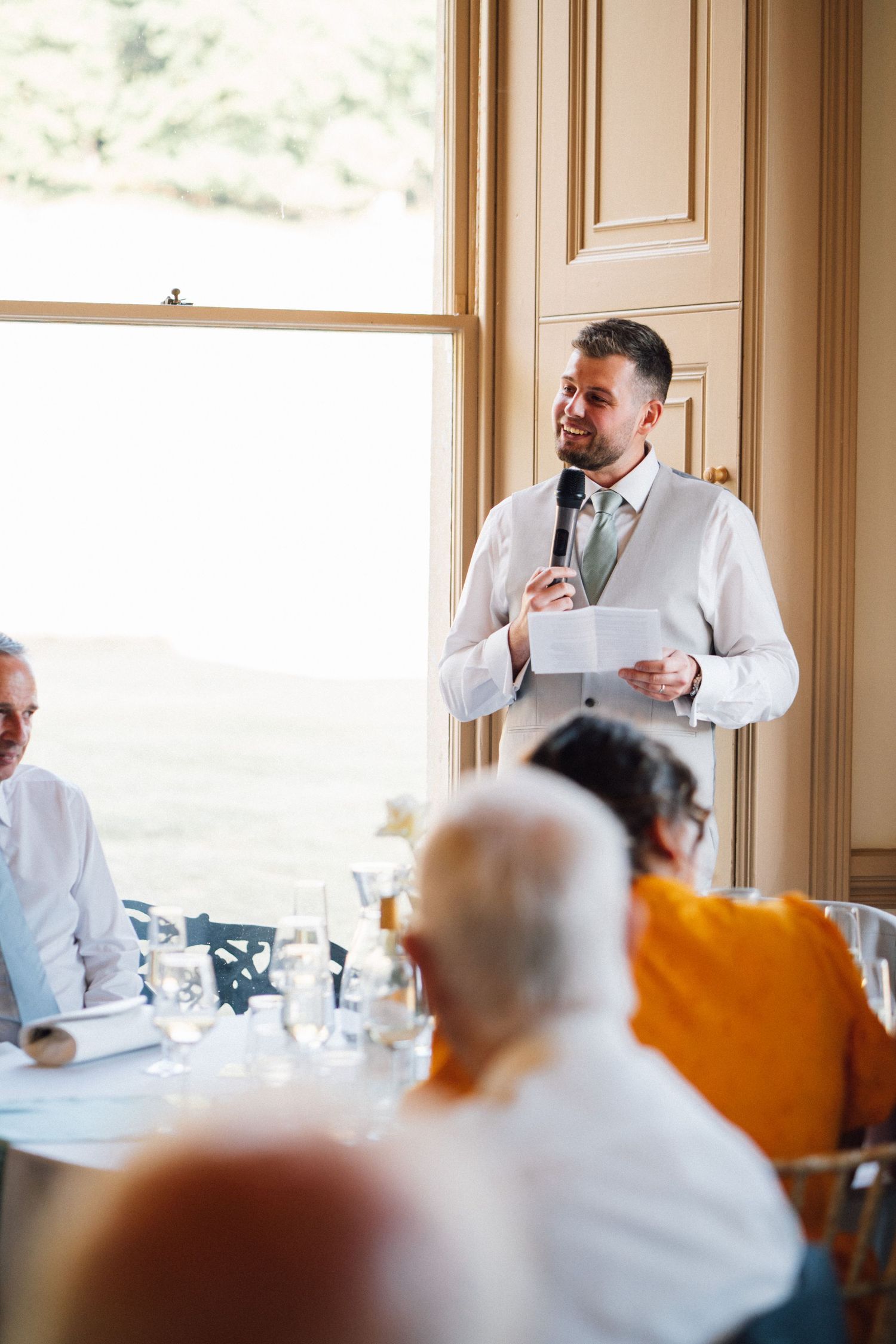 Wedding reception speech being given in a sunlit room with formal table settings.