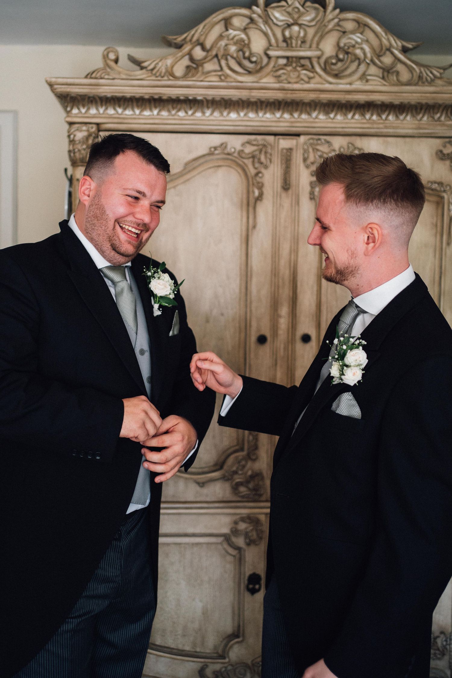 Two people share a joyful moment exchanging rings in front of an ornate vintage armoire.