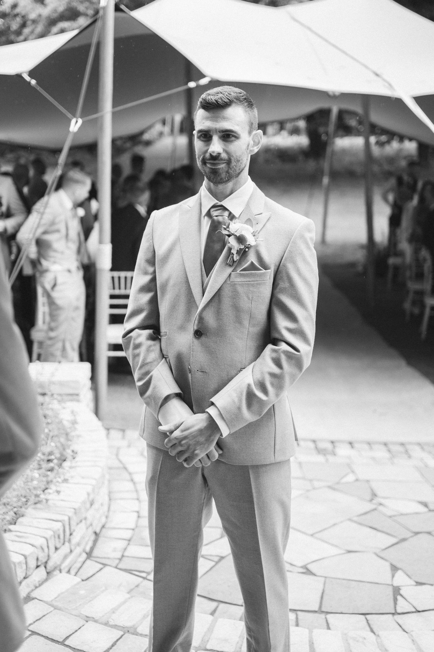 Black and white photo of groomsmen in light colored suits standing on stone patio at outdoor wedding venue.