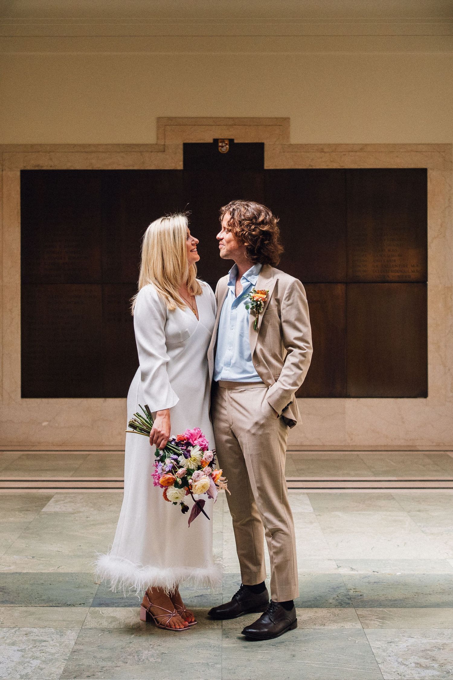 A romantic wedding photo series showing a couple in white dress and tan suit embracing against a neutral wall backdrop.