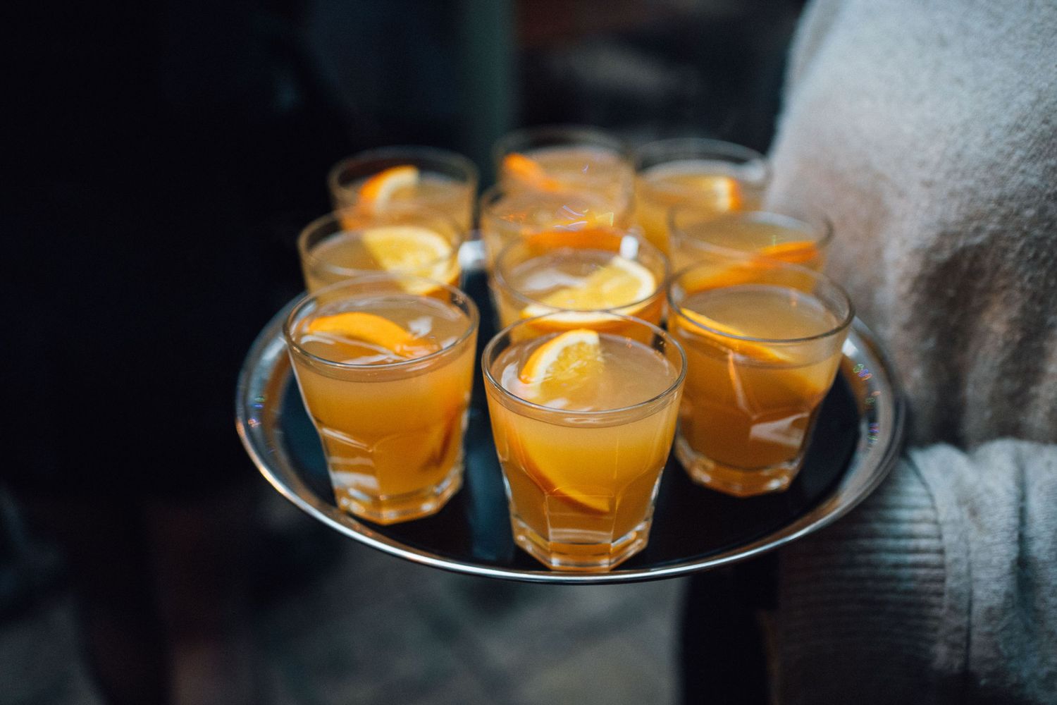 Small glass cups filled with orange-colored cocktails garnished with citrus slices on a dark surface.