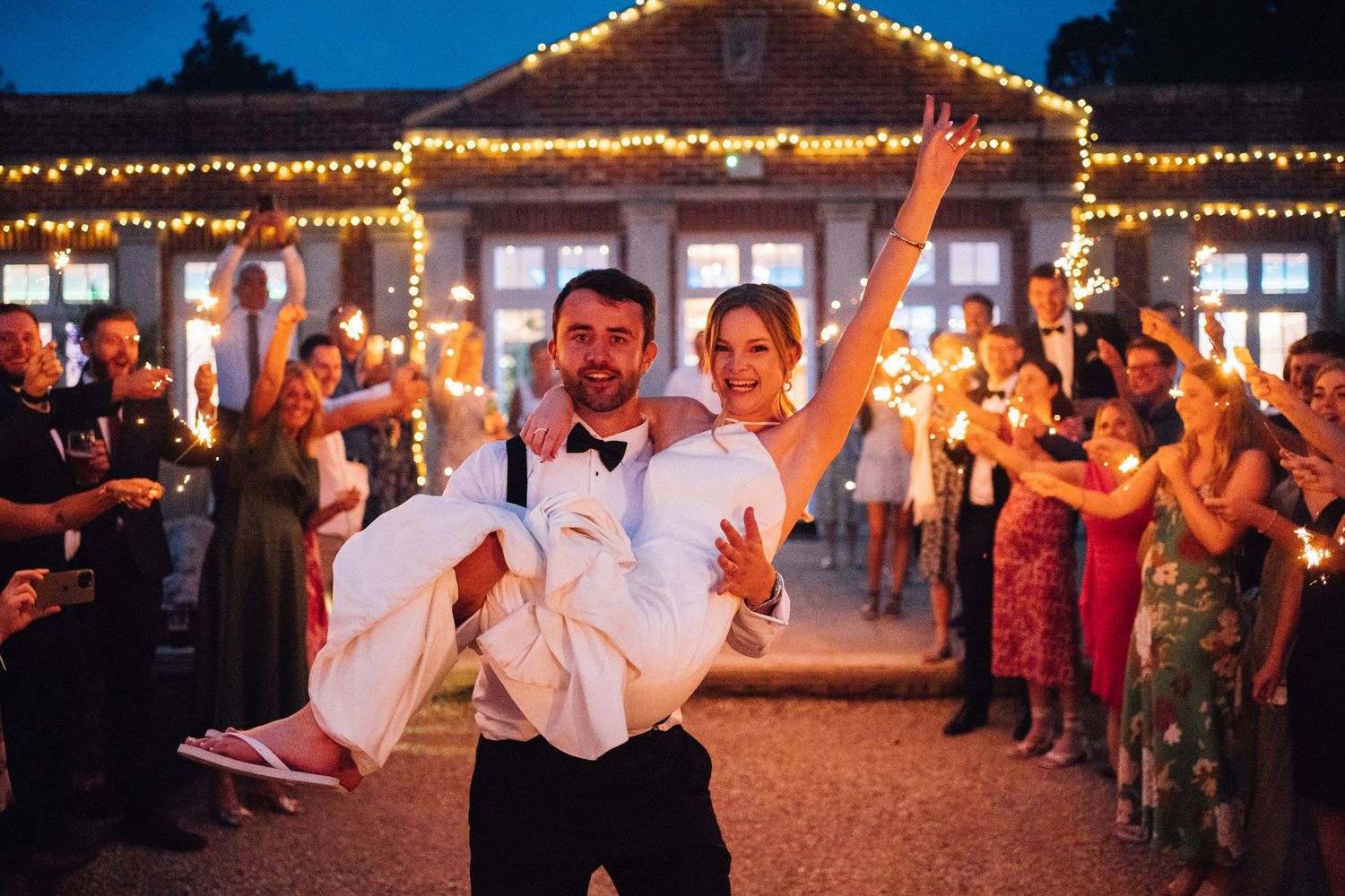 Wedding reception at night with string lights illuminating guests dancing and celebrating on an outdoor patio.