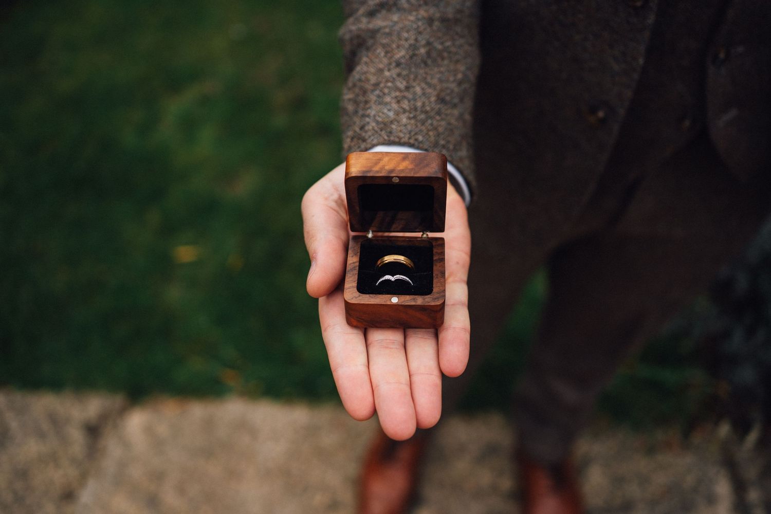 A close-up shot of a small ring box being opened in an outdoor garden setting.