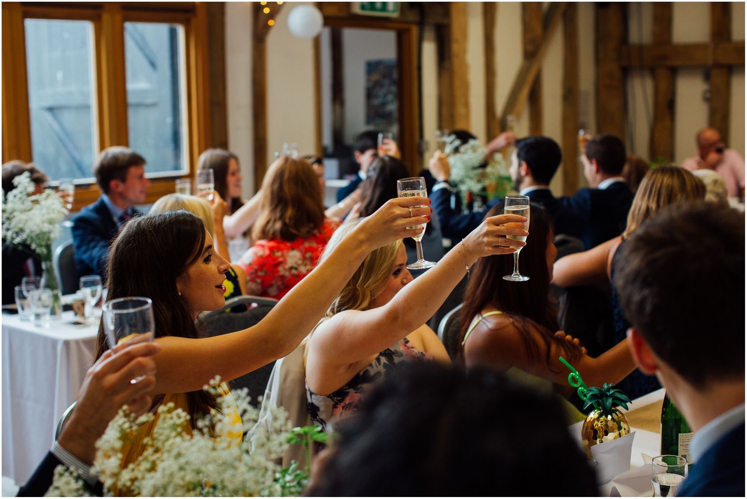 Wedding guests raising glasses for toast during indoor reception celebration.
