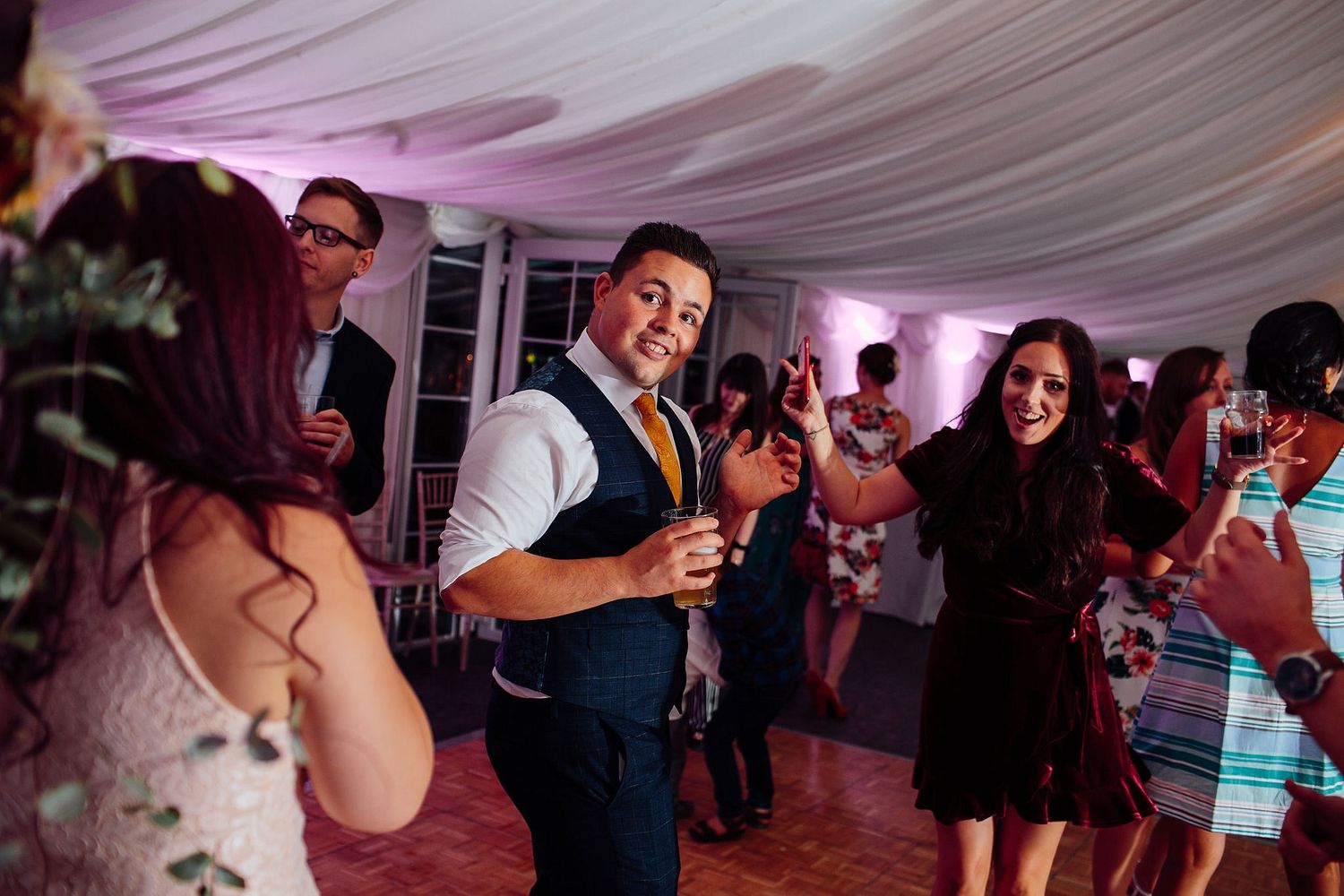 Guests dance and celebrate at a wedding reception under pink mood lighting.