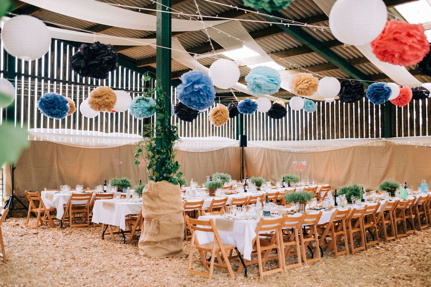 Wedding reception venue decorated with hanging paper lanterns and wooden chairs.