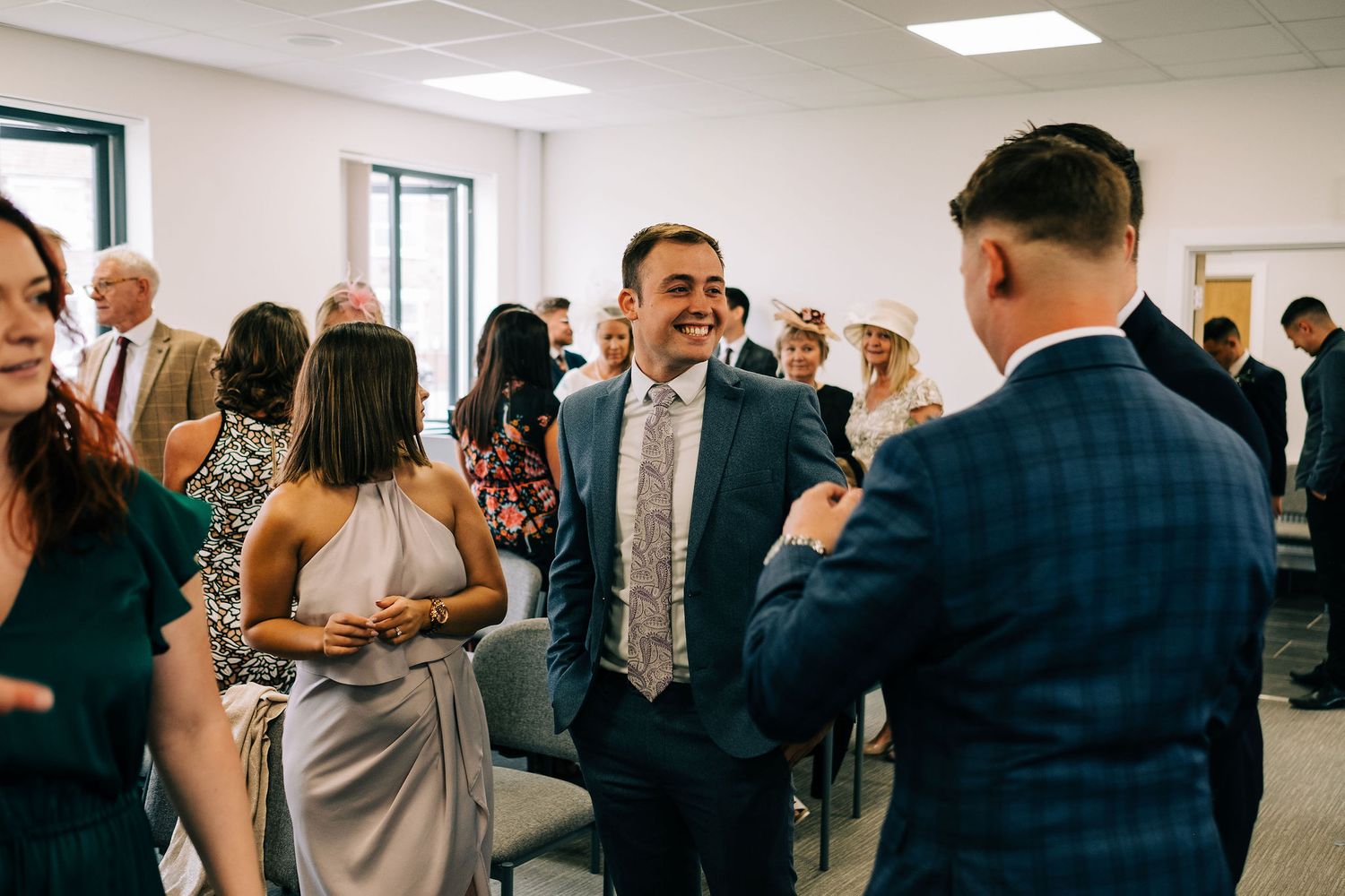 Wedding guests socializing and celebrating in a bright indoor reception space.