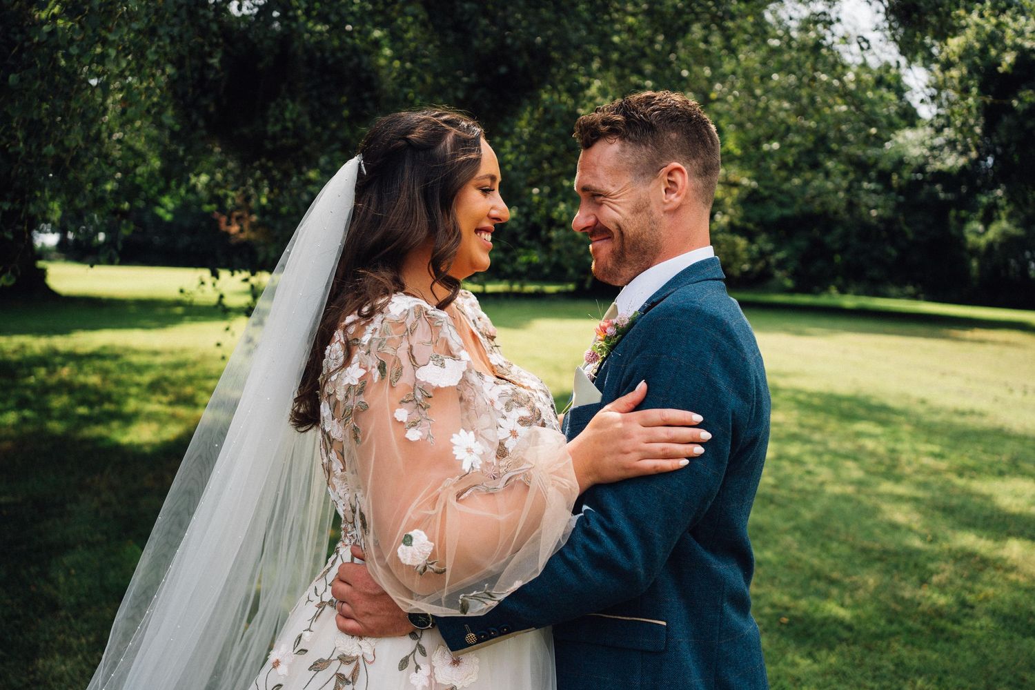 Intimate moment between newlyweds sharing laughter in a sunny garden setting.