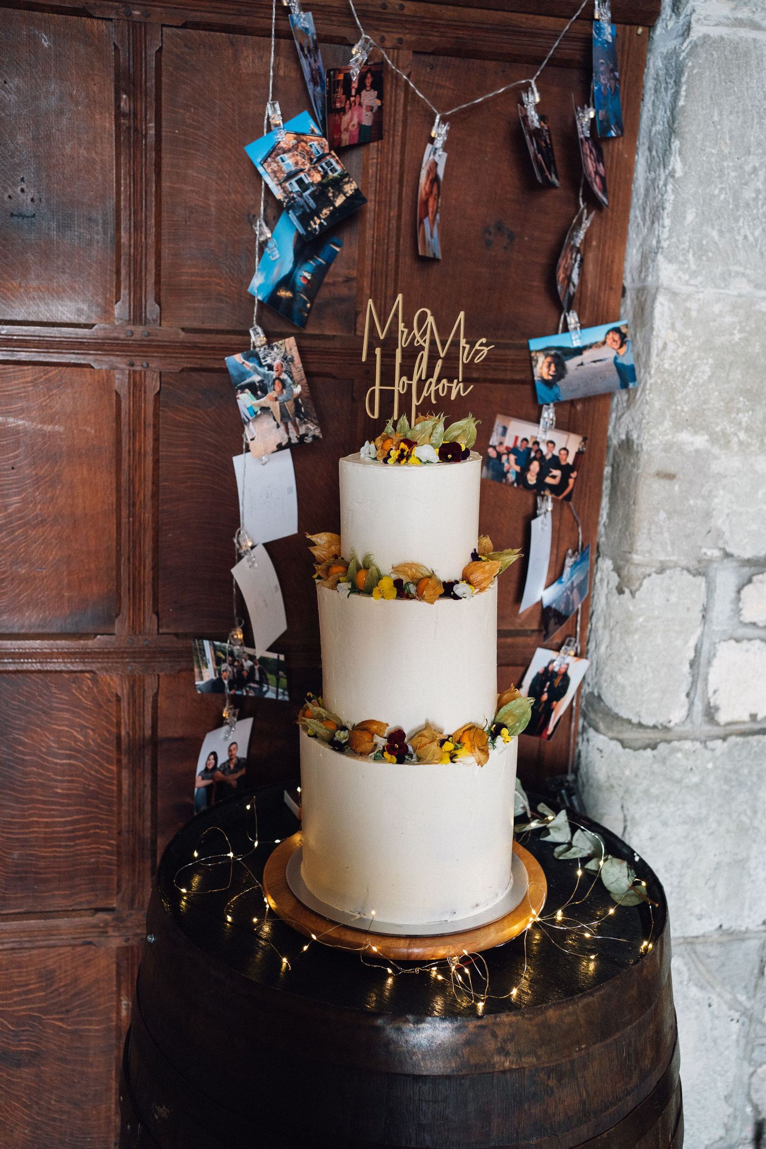 Three-tiered white wedding cake decorated with photos and blue accents against wooden paneling.