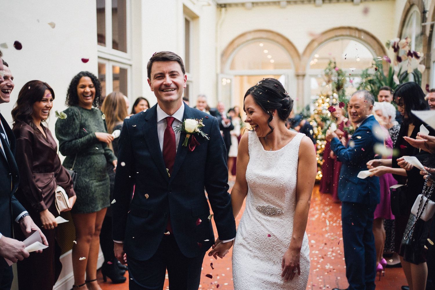 Wedding party walks through a grand hallway while guests shower them with confetti.
