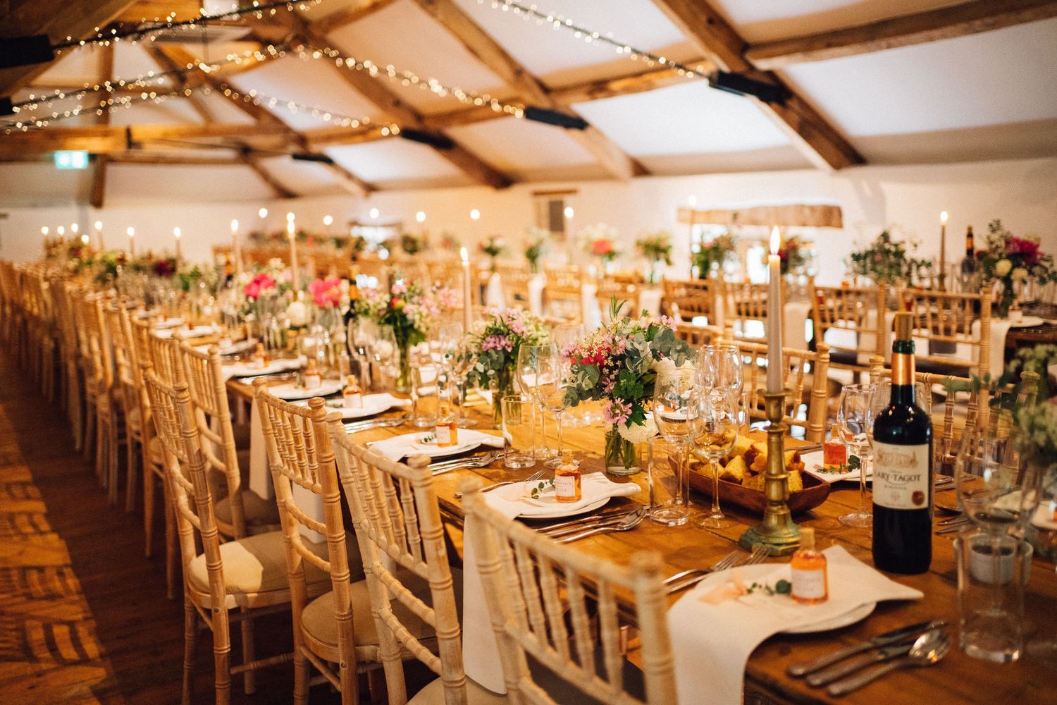 Rustic barn reception venue with wooden beams and twinkling lights creating a warm ambiance.