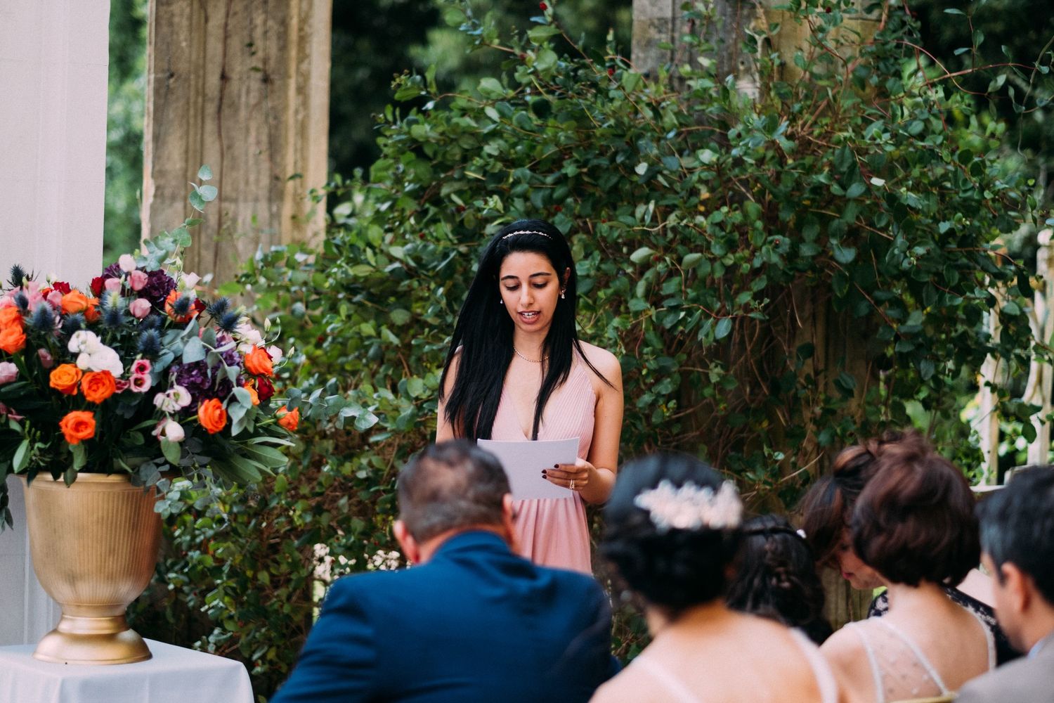 An outdoor wedding ceremony with decorative orange flowers and classical architecture.
