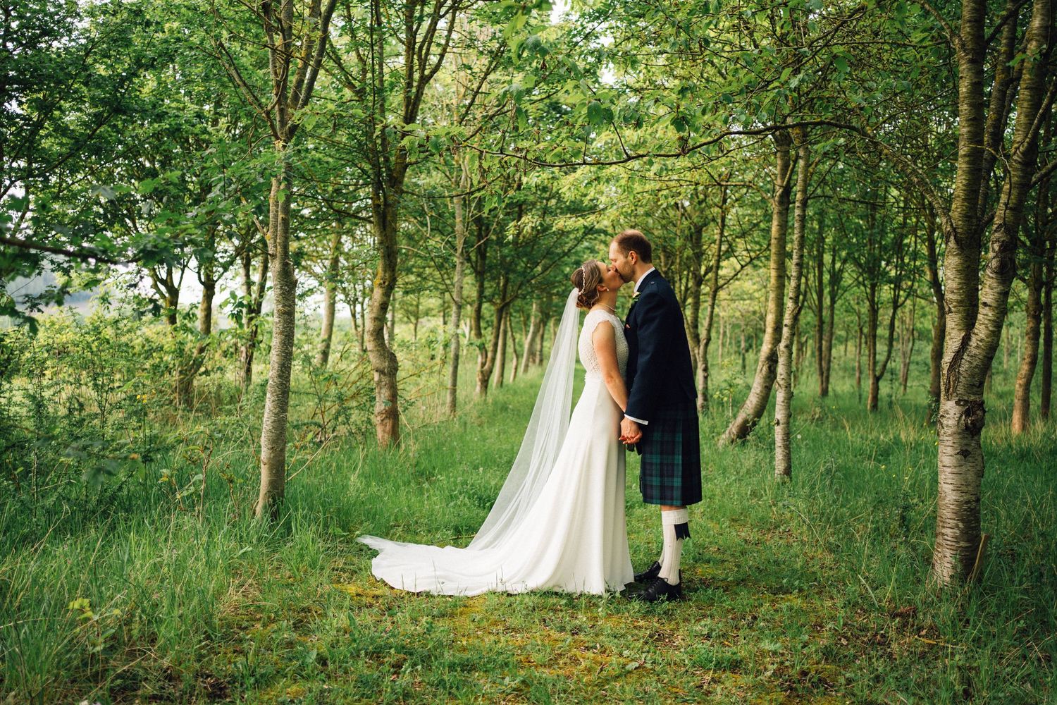 Couple poses for romantic wedding portrait in a sunlit forest setting.