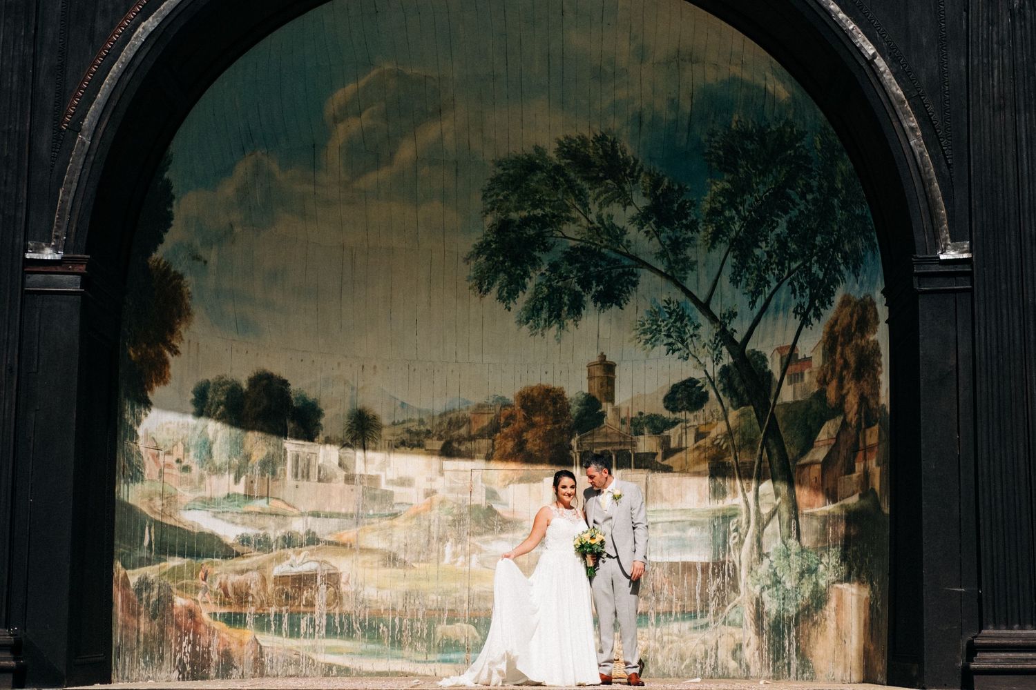 Elegant wedding portrait against a scenic painted mural backdrop.