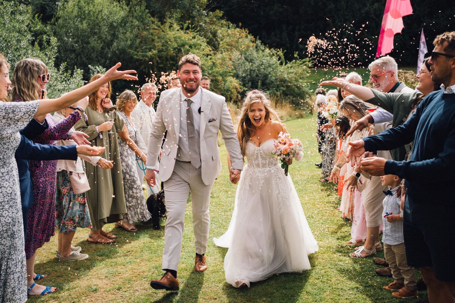 Wedding guests form a line outdoors throwing confetti in celebration.