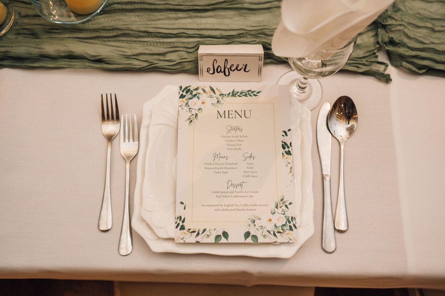 Elegant place settings with floral menu cards and gold silverware arranged on a white tablecloth at a formal event.