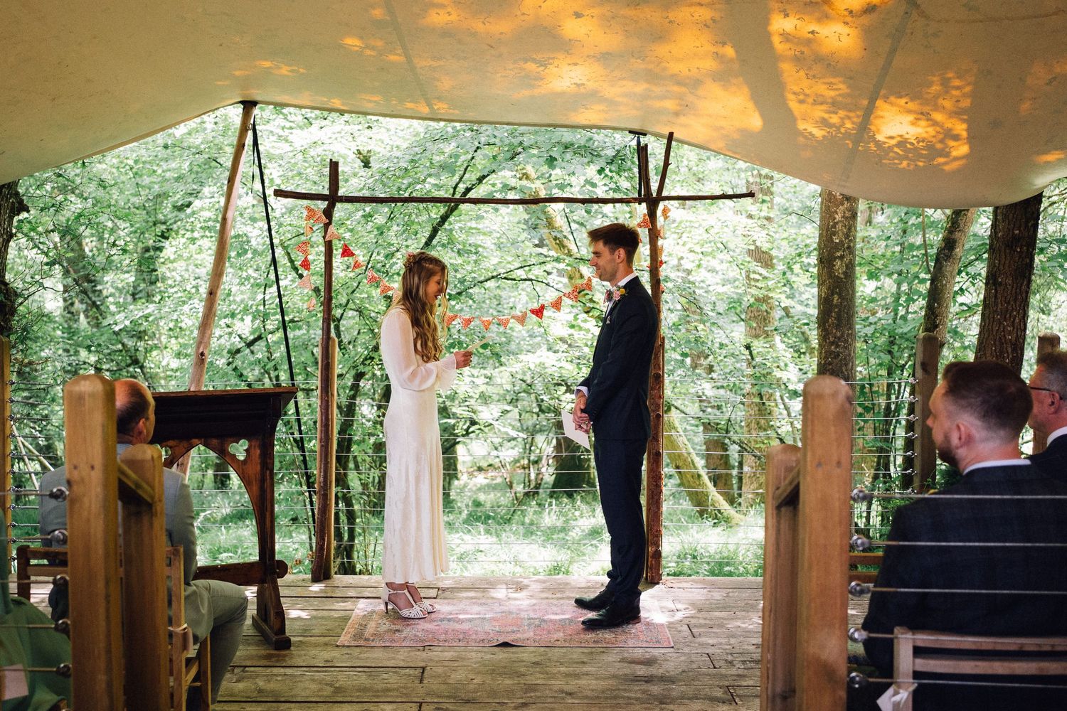 A couple shares a romantic moment during their outdoor forest wedding ceremony at sunset with golden light filtering through trees.