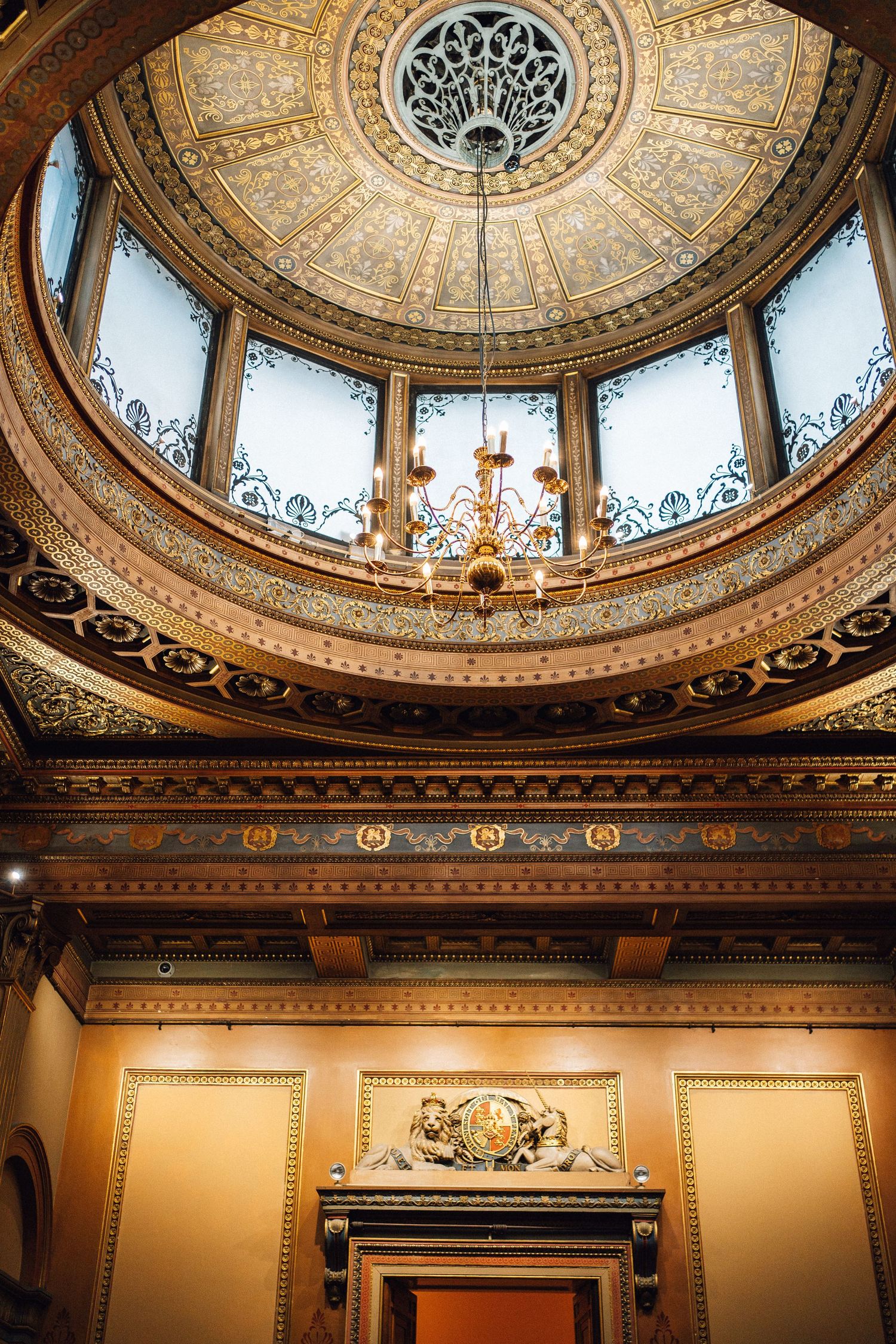 Ornate architectural details of a grand domed ceiling with intricate moldings and decorative patterns in warm golden tones.