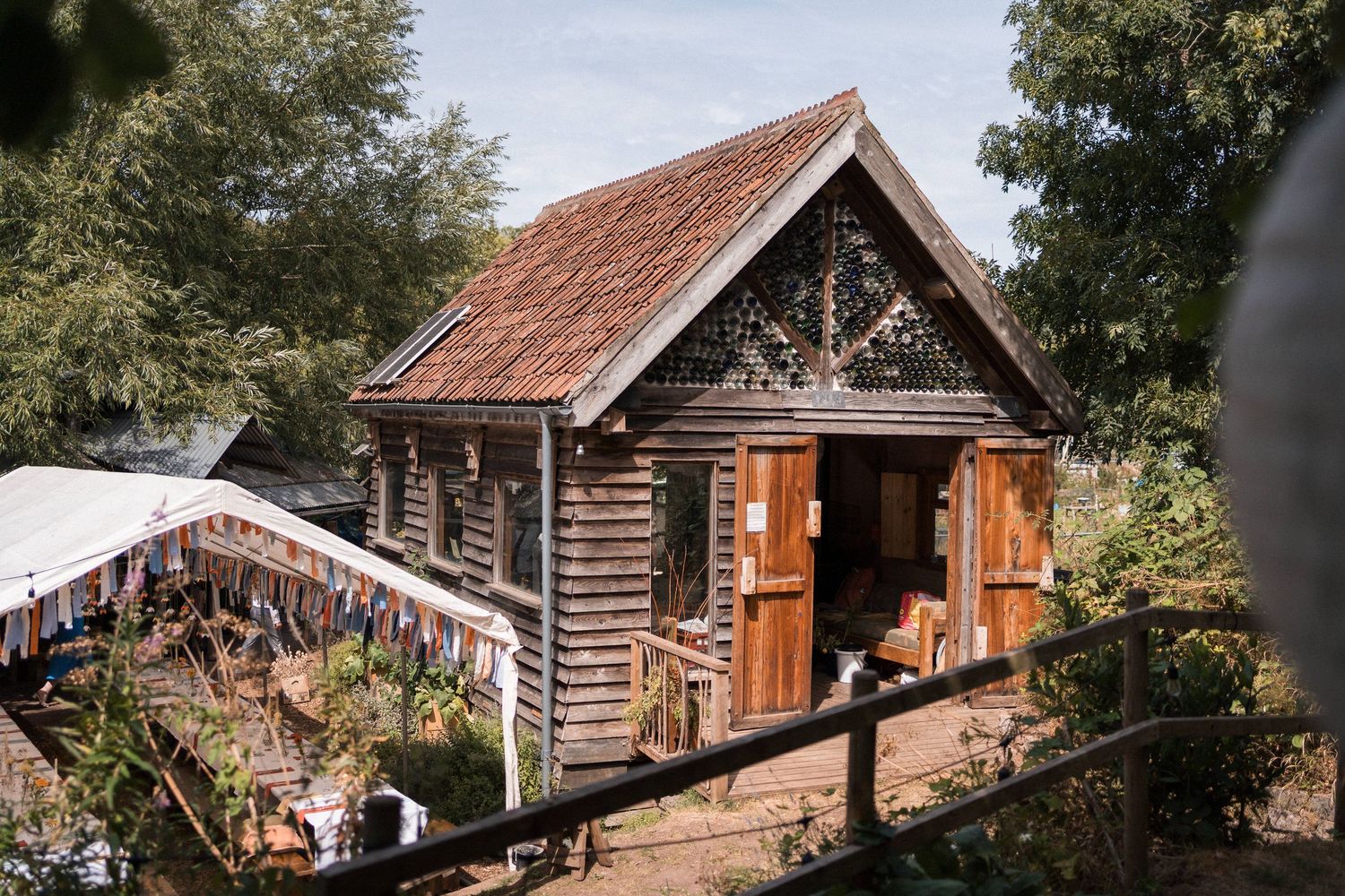 Rustic wooden log cabin with terracotta roof tiles surrounded by lush trees and colorful bunting flags.