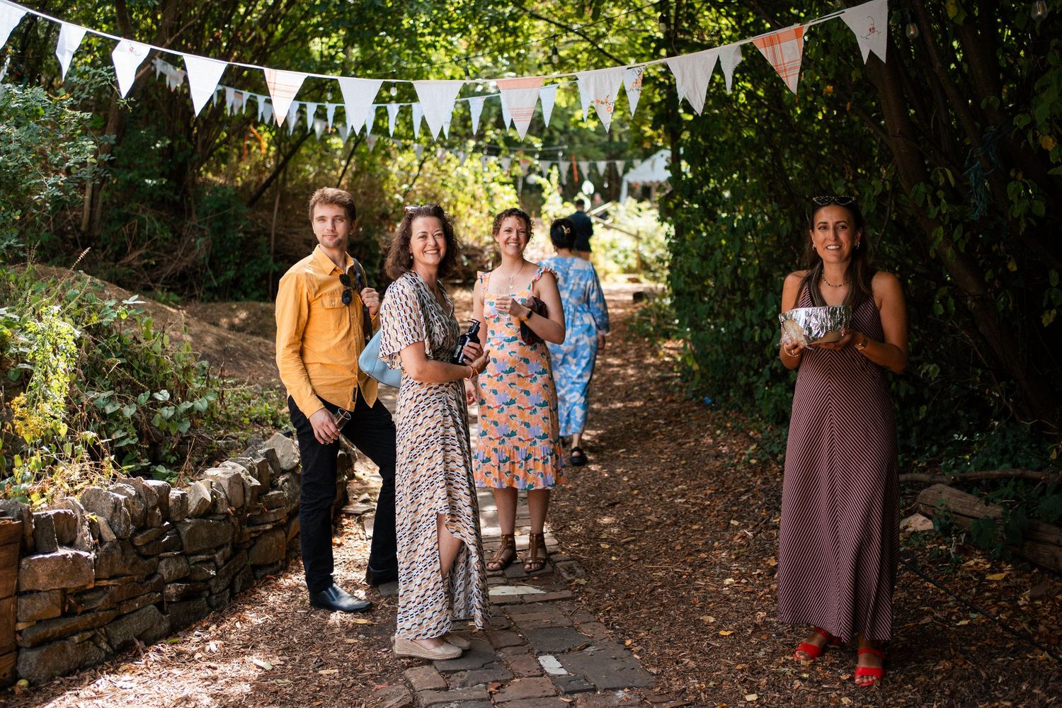 Group of five people celebrating outdoors in a garden party setting with bunting decorations and lush greenery.