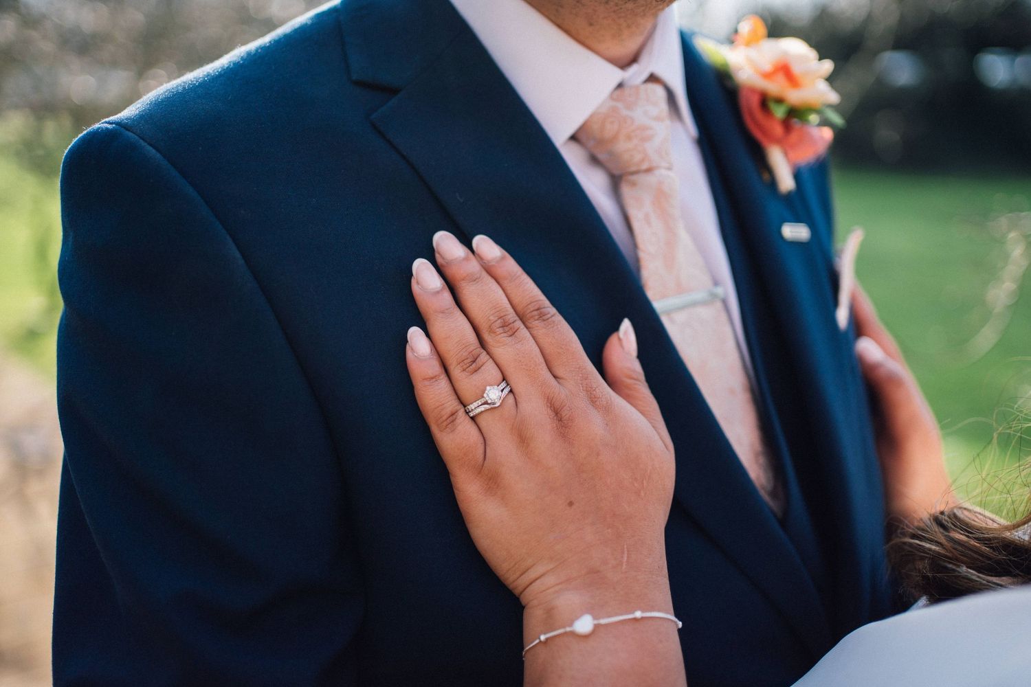 Close-up details of wedding couple showing rings, jewelry and formal attire.